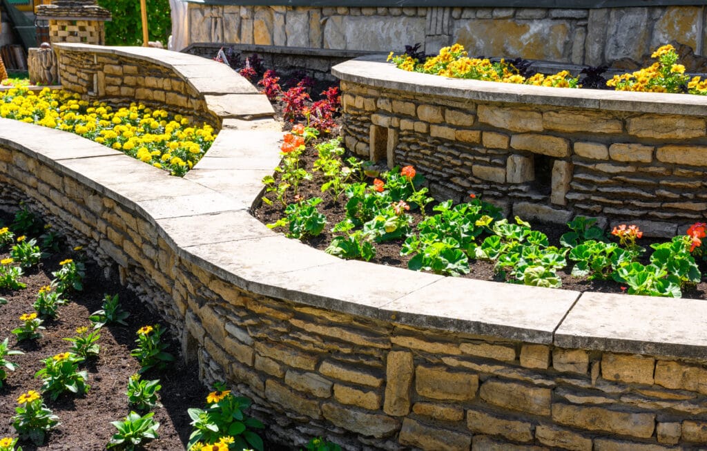 Retaining walls featuring many planted flowers, example of summer hardscaping and hardscape design.