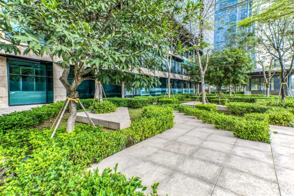 Gray building with blue windows with patio containing small trees and hedges. Example of commercial landscaping maintenance services.