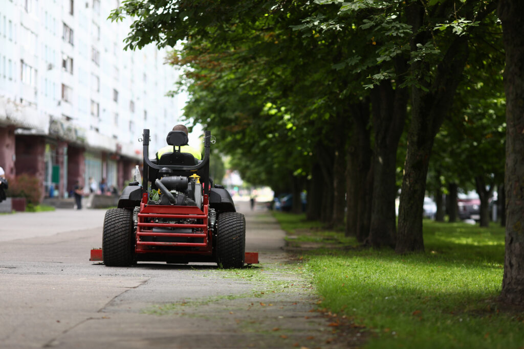 Lawnmower riding down sidewalk lined with trees, example of commercial landscaping maintenance services.