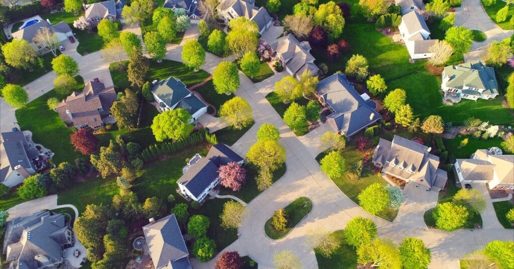 Aerial view of suburban hoa neighborhood landscaping with curved streets, houses surrounded by green lawns, and many trees with fresh spring foliage.