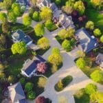 Aerial view of suburban hoa neighborhood landscaping with curved streets, houses surrounded by green lawns, and many trees with fresh spring foliage.