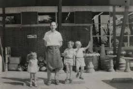 A black-and-white photo of a man in an apron standing outside Walnut Ridge with three children, the original family of the local landscaping company.